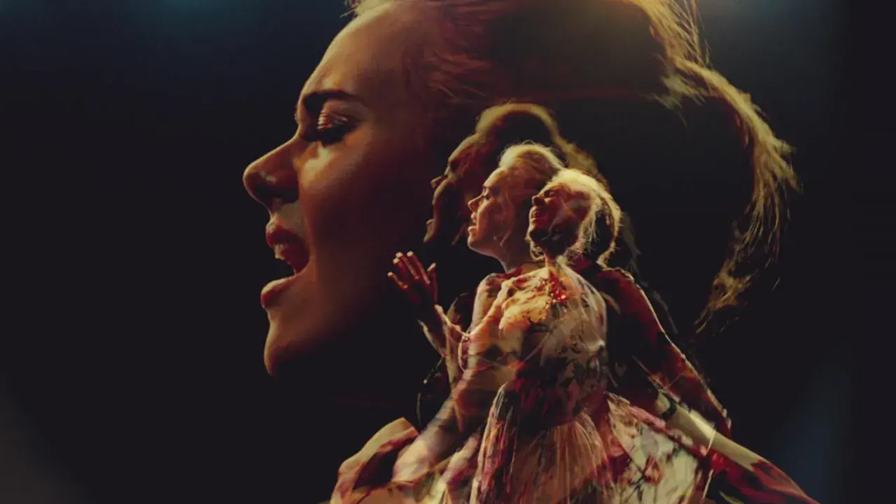 Adele śpiewa "Send My Love" w wielokrotnej ekspozycji, jej twarz i postać w sukni rozmywają się w mroku.