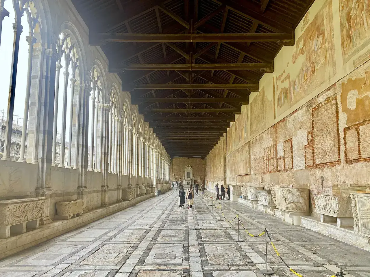Corridoio del Camposanto Monumentale di Pisa con arcate gotiche, affreschi antichi e sarcofagi romani.