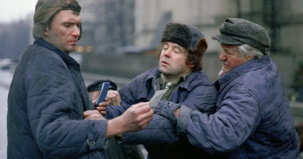 Trzech mężczyzn w zimowych kurtkach i czapkach, w tym jedna z futrzanymi uszami, dyskutuje, trzymając w rękach dokumenty. Scena z filmu "Miś" z niezapomnianą obsadą.