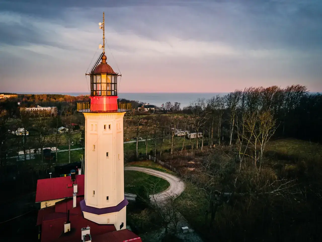 Najstarsza latarnia morska w Polsce, wysoka, kremowa wieża z czerwonymi akcentami, góruje nad krajobrazem o zachodzie słońca.