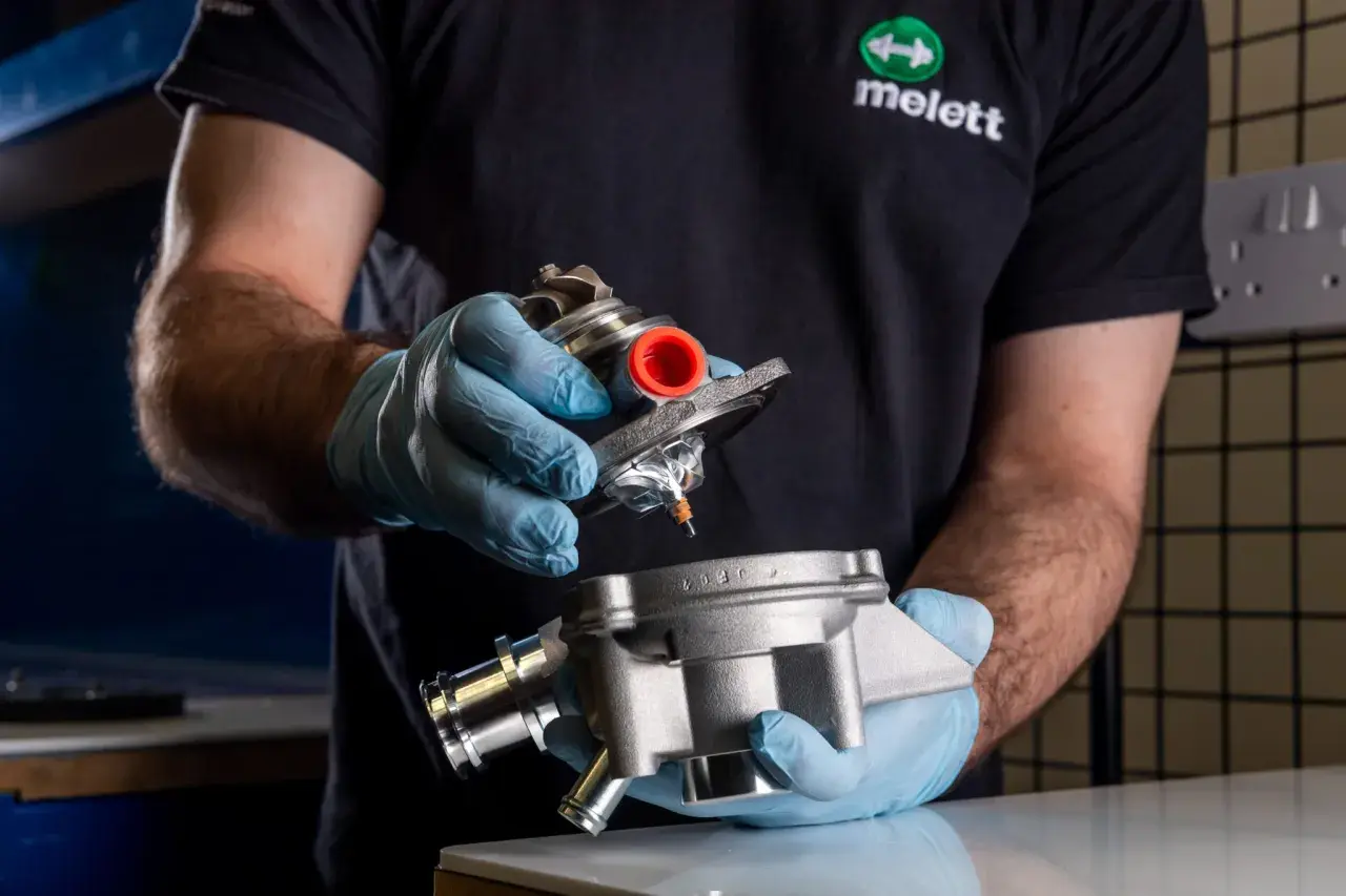 Mano con guante azul sostiene un turbo y su carcasa, inspeccionando posible perdida de aceite por el turbo.