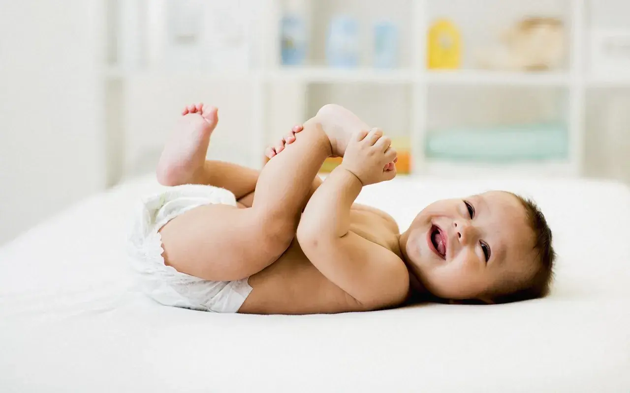 Bambino sorridente in pannolino gioca con i piedini, felice dopo aver fatto la cacca neonato.