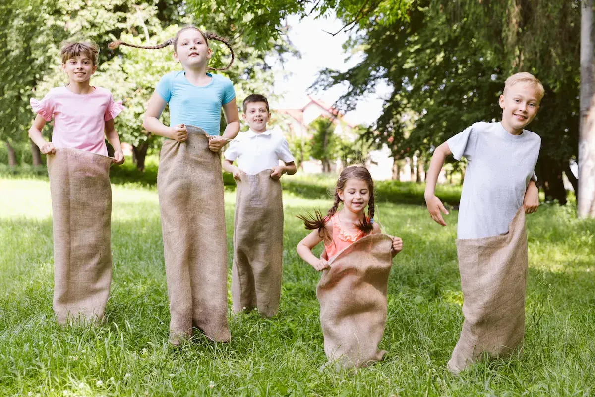 Niños compiten en carreras de sacos en un día soleado, disfrutando en familia de juegos al aire libre.