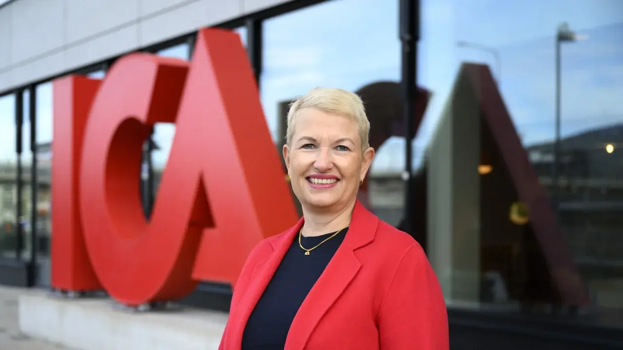 En leende kvinna i röd kavaj framför stora röda bokstäver som bildar ICA. Hon är ICA:s VD.