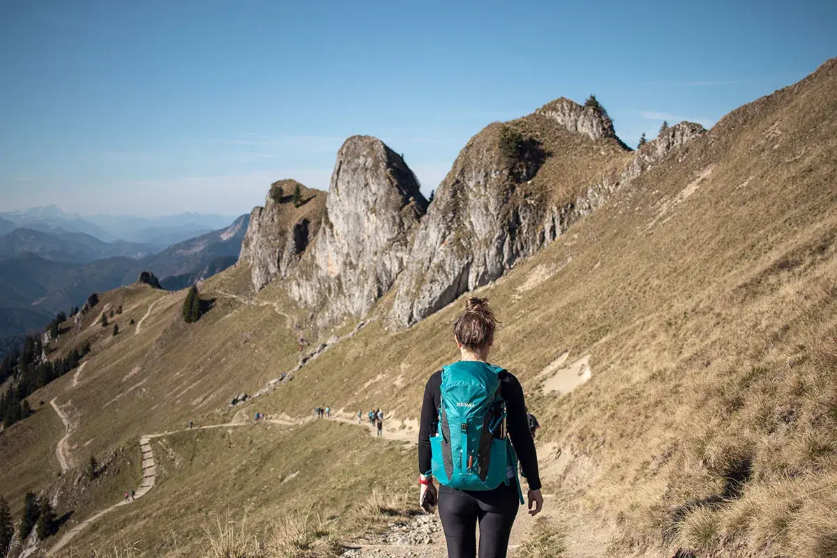 Wanderin auf einem Pfad in den beeindruckenden Berge in Bayern. Die Sonne scheint, der Himmel ist blau.