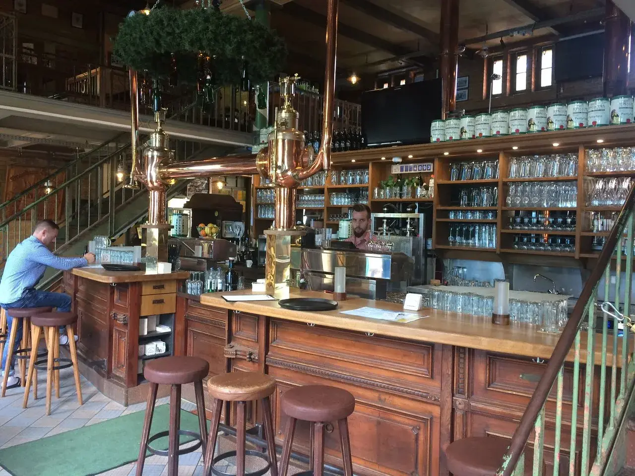 Gemütliche Atmosphäre im Brauhaus Spandau. Ein Mann sitzt am Tresen, hinter ihm Regale voller Gläser und Bierfässer.