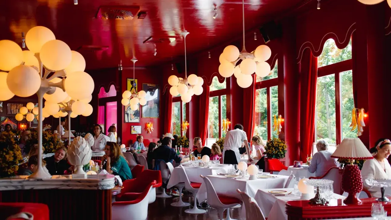 Ein lebhaftes **Cafe Berlin Mitte** mit roten Wänden, auffälligen Kugelleuchten und Gästen, die an weiß gedeckten Tischen sitzen.