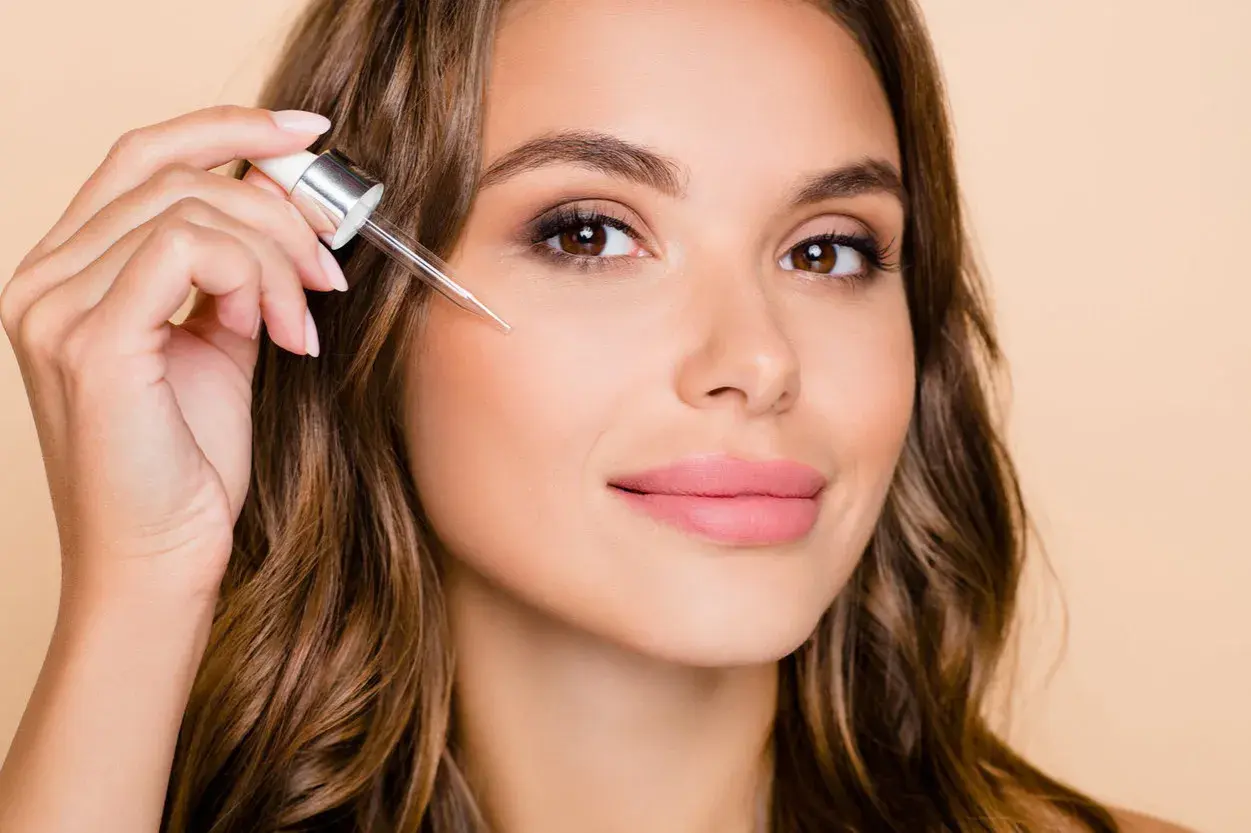 Kobieta aplikuje serum z pipetki na policzek. Dowiedz się, jak stosować retinol dla pięknej cery.