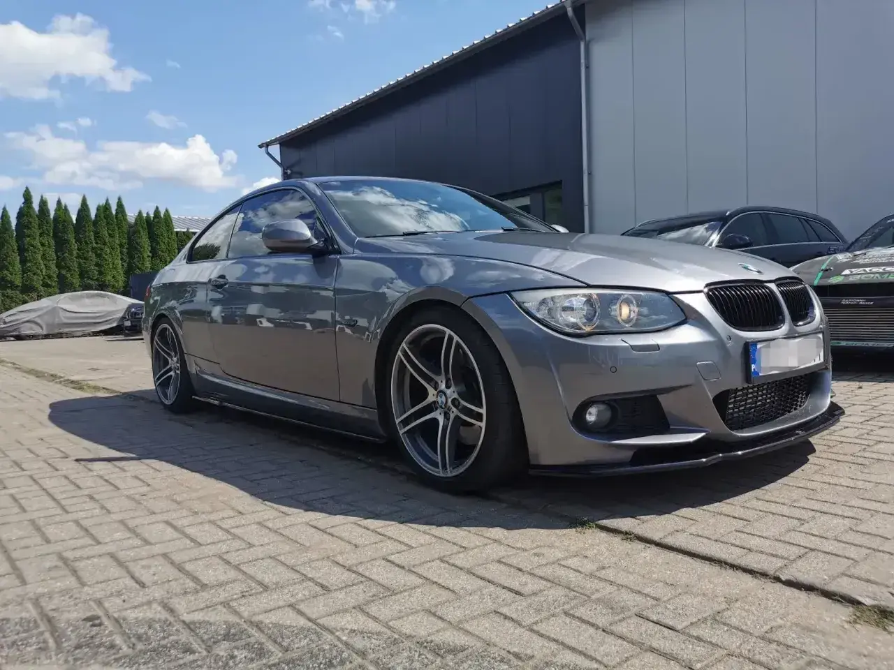 Szare BMW E92 335d z przyciemnianymi szybami i sportowym dyfuzorem, zaparkowane na zewnątrz.