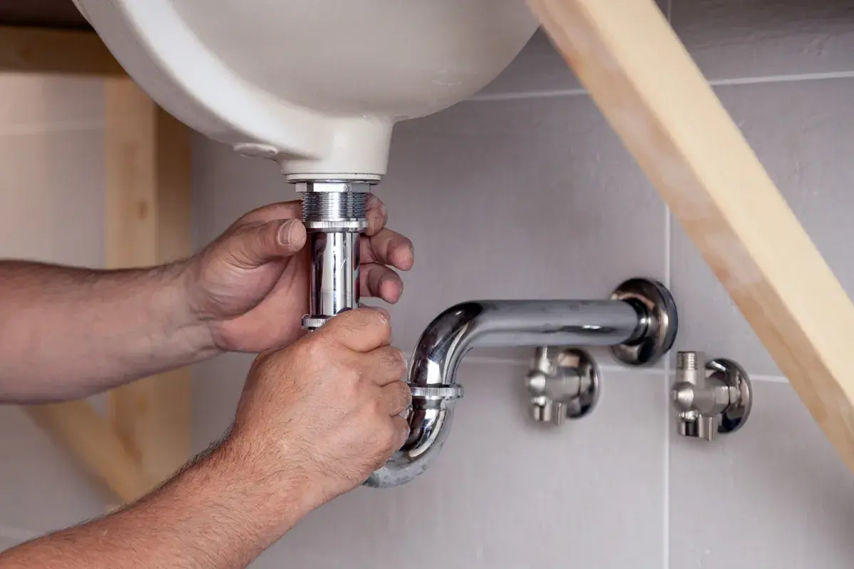 Hände schrauben am Siphon unter dem Waschbecken. Ein Handwerker reinigt den Siphon, um Verstopfungen zu beseitigen.