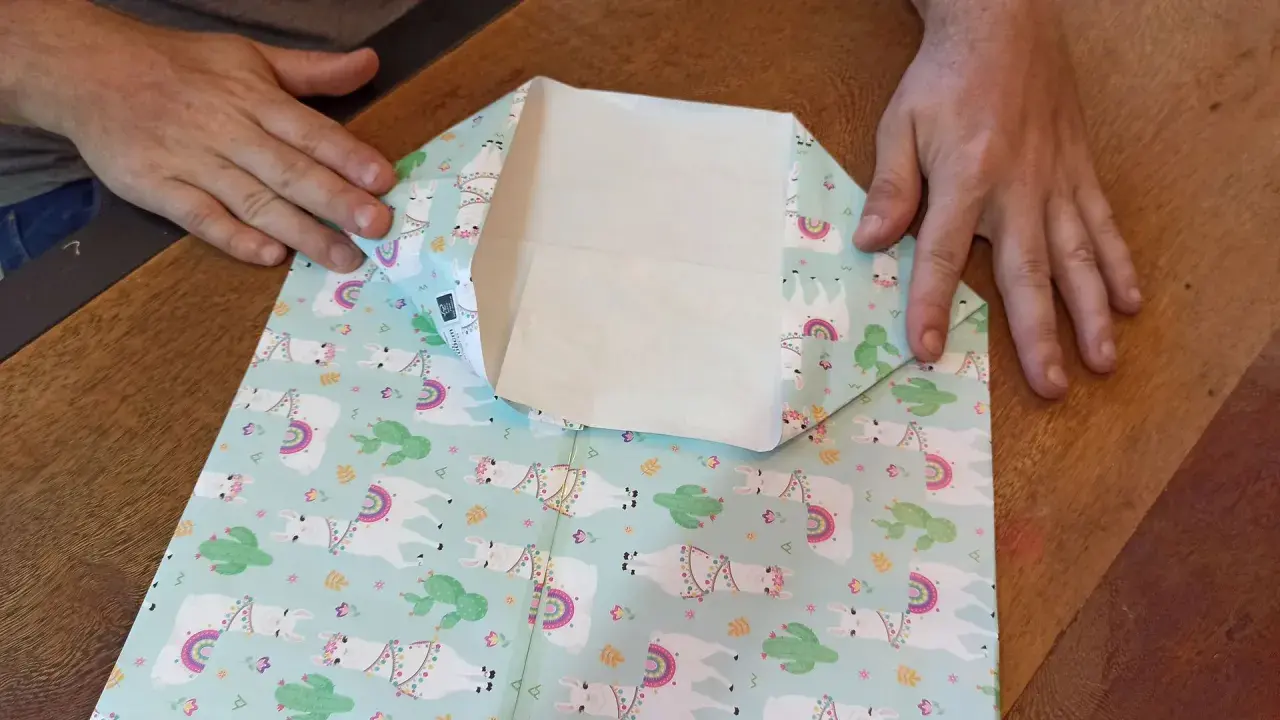 Mani che piegano carta regalo con lama e cactus per creare mini sacchetti di carta fai da te.