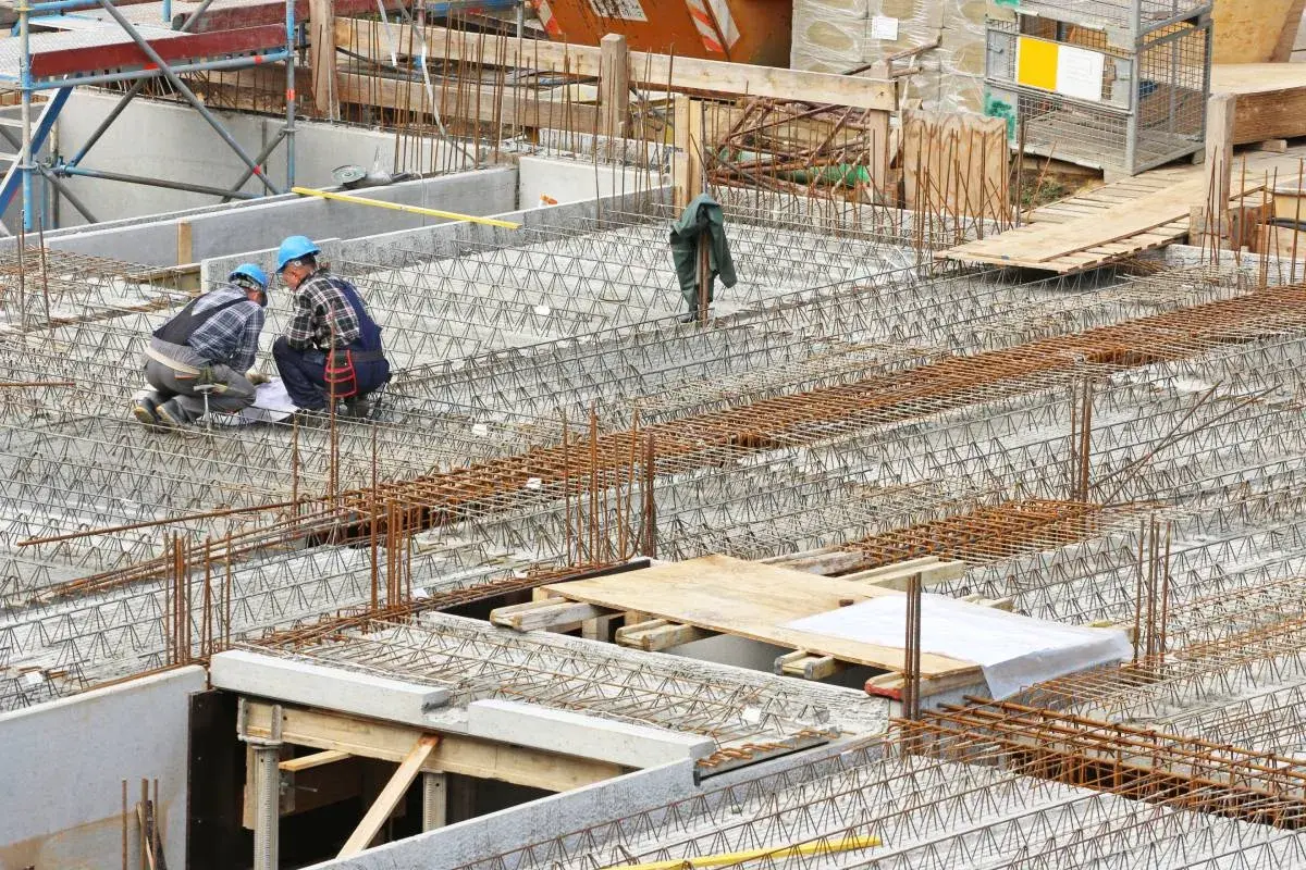 Bauarbeiter prüfen Pläne für verschiedene betondecken arten. Stahlbewehrung für eine massive Betonplatte ist sichtbar.