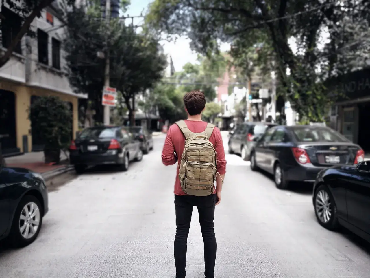 Ein junger Mann mit Rucksack steht auf einer Straße in Mittelamerika, bereit für sein nächstes Abenteuer beim Backpacking.