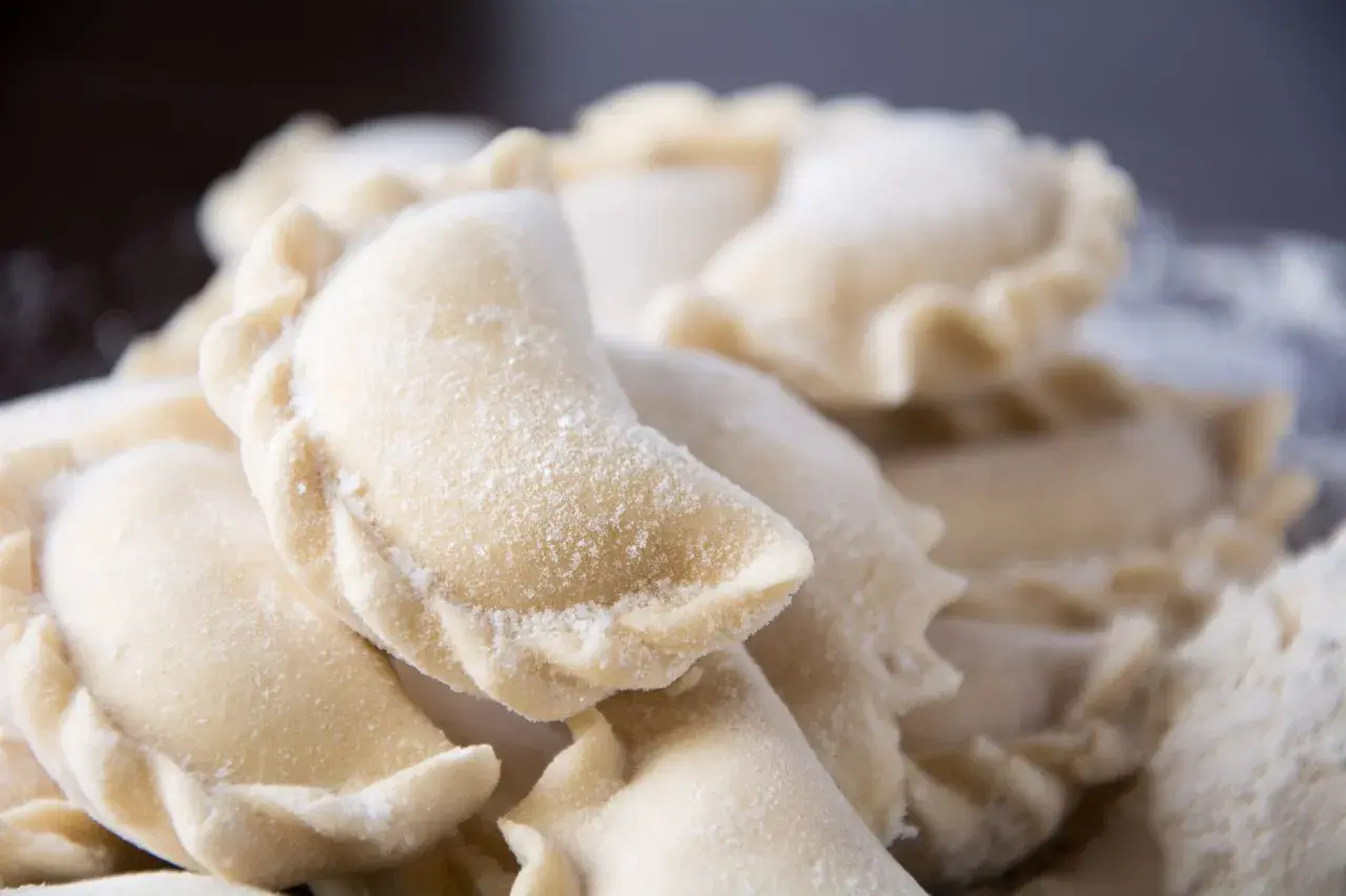 Zbliżenie na surowe, mrożone pierogi posypane mąką.