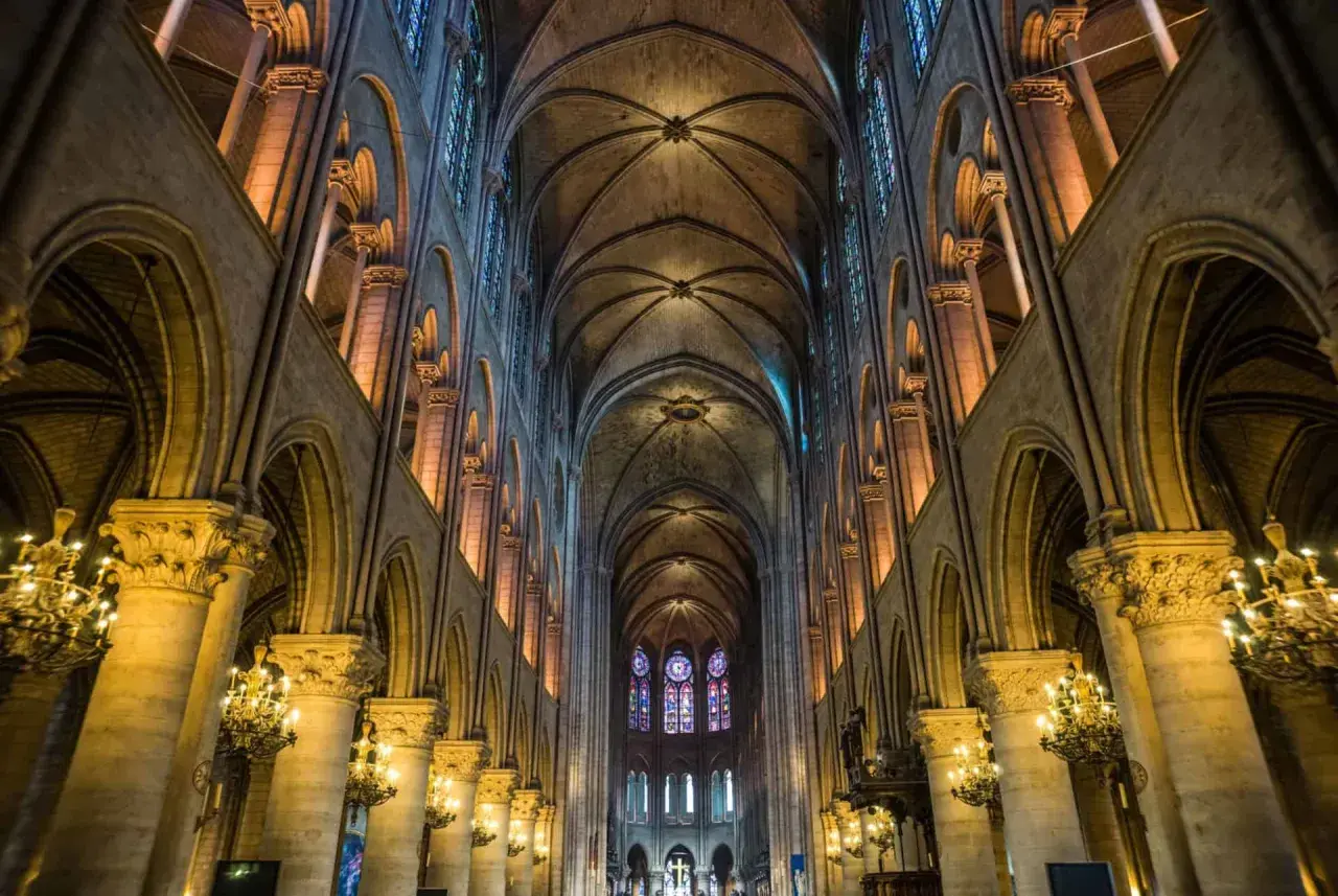 Intérieur de Notre Dame de Paris, avec ses voûtes gothiques, vitraux colorés et chandeliers. On se demande si peut on visiter Notre Dame de Paris.