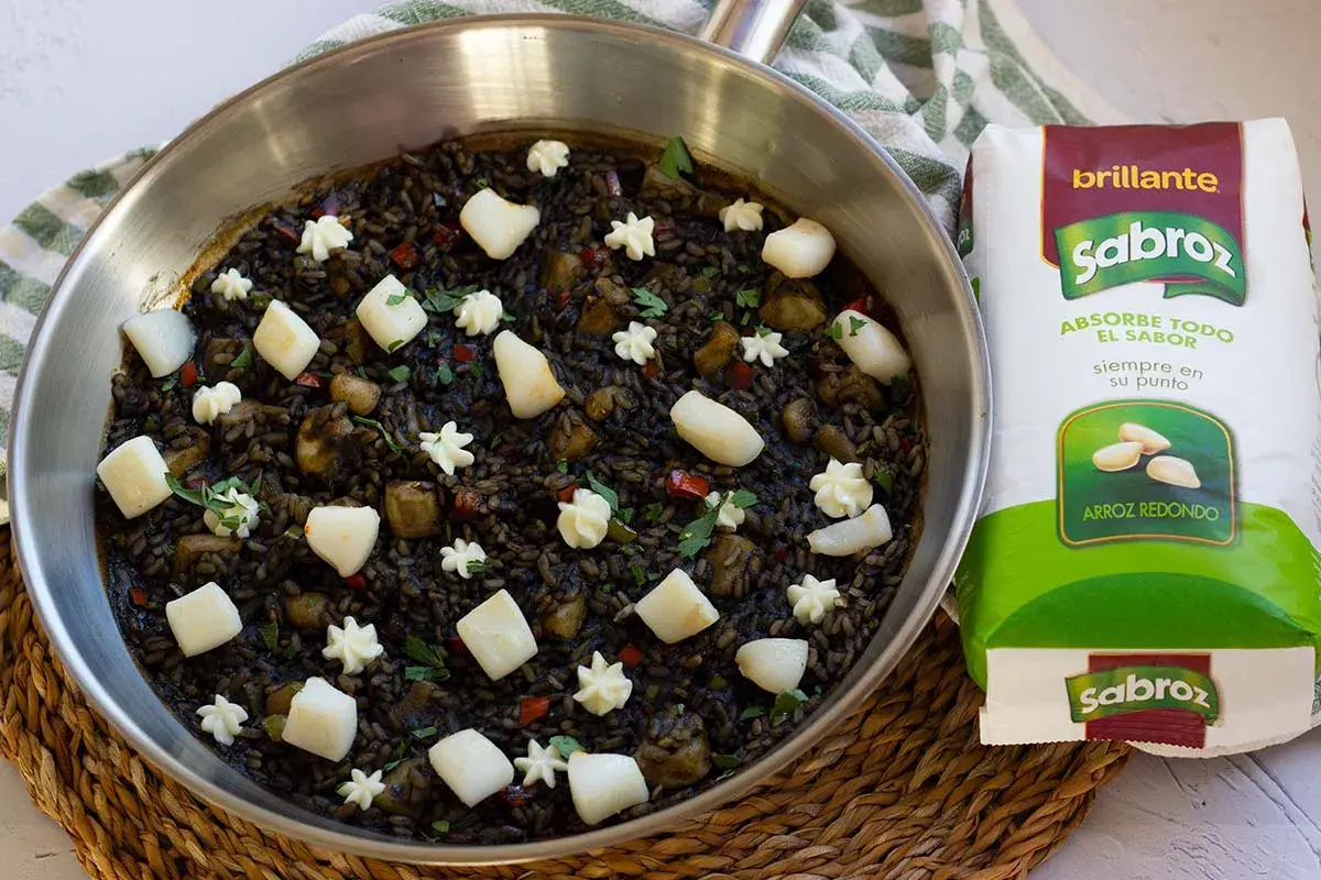 Arroz negro con sepia, adornado con trozos de sepia y puntos de alioli, listo para ser cocinado con arroz redondo Sabroz.