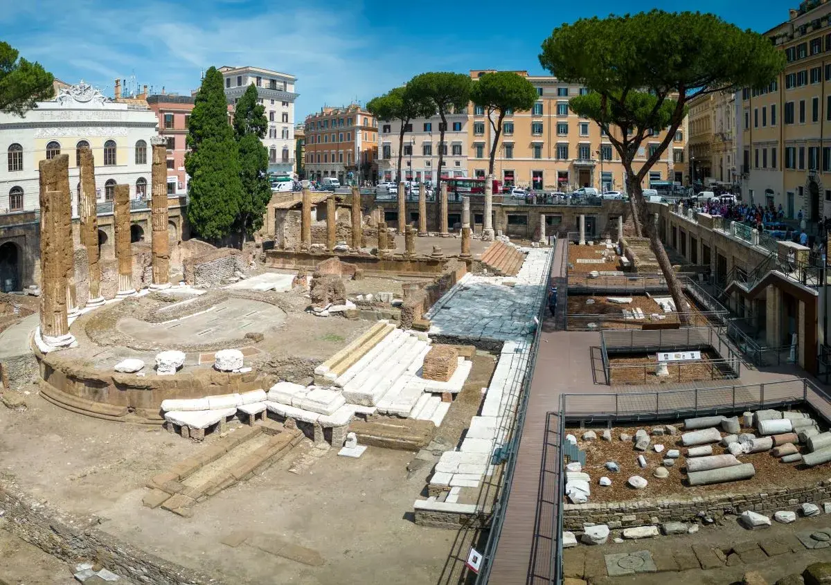 Antiche rovine dell'area sacra di Largo Argentina a Roma, con colonne e resti di templi sotto un cielo azzurro.