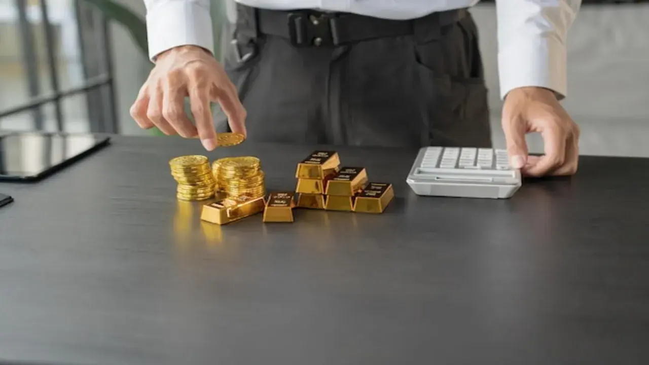 Ręce układają stosy złotych monet i sztabek, obok kalkulator. To inwestycja w złoto Heraeus.