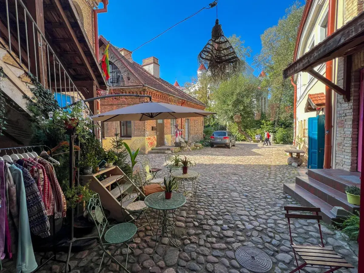 Urokliwy dziedziniec w Wilnie, z kawiarnianymi stolikami i wieszakami z ubraniami, zaprasza na wieczorne atrakcje.
