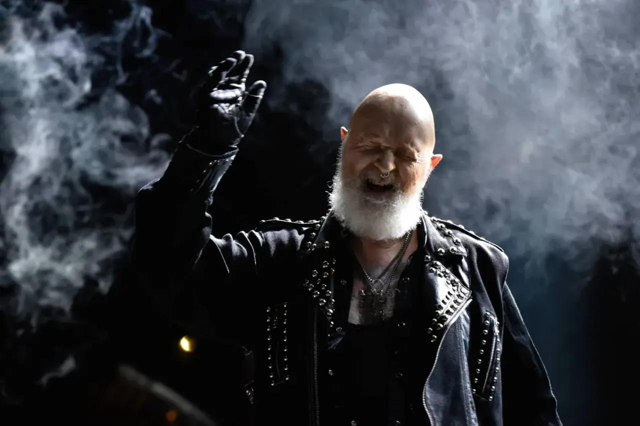 Rob Halford z Judas Priest, w skórzanej kurtce z ćwiekami, wznosi rękę w geście, jakby wykrzykując "Panic Attack" na koncercie.