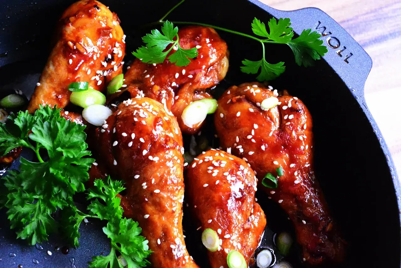 Kurczak teriyaki w glazurze z sezamem i szczypiorkiem w czarnej patelni.
