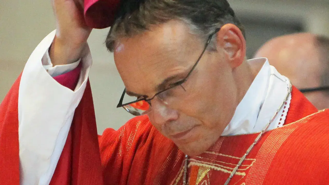 Bischof Tebartz van Elst trägt eine rote Messrobe und eine weiße Halskrause. Er blickt nach unten, während er eine Kopfbedeckung aufsetzt.