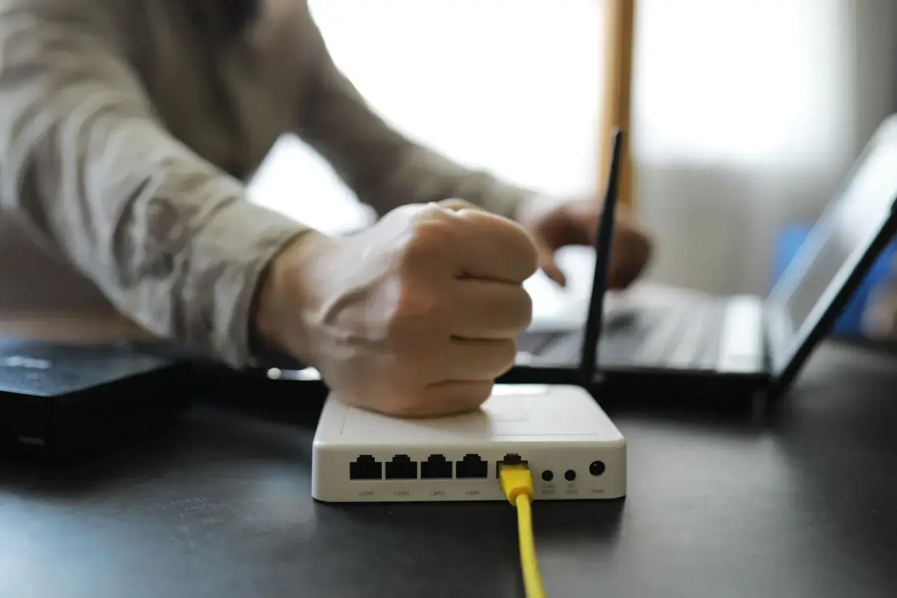Zirytowany użytkownik próbuje dowiedzieć się, jak przyspieszyć ethernet, patrząc na router i laptopa.