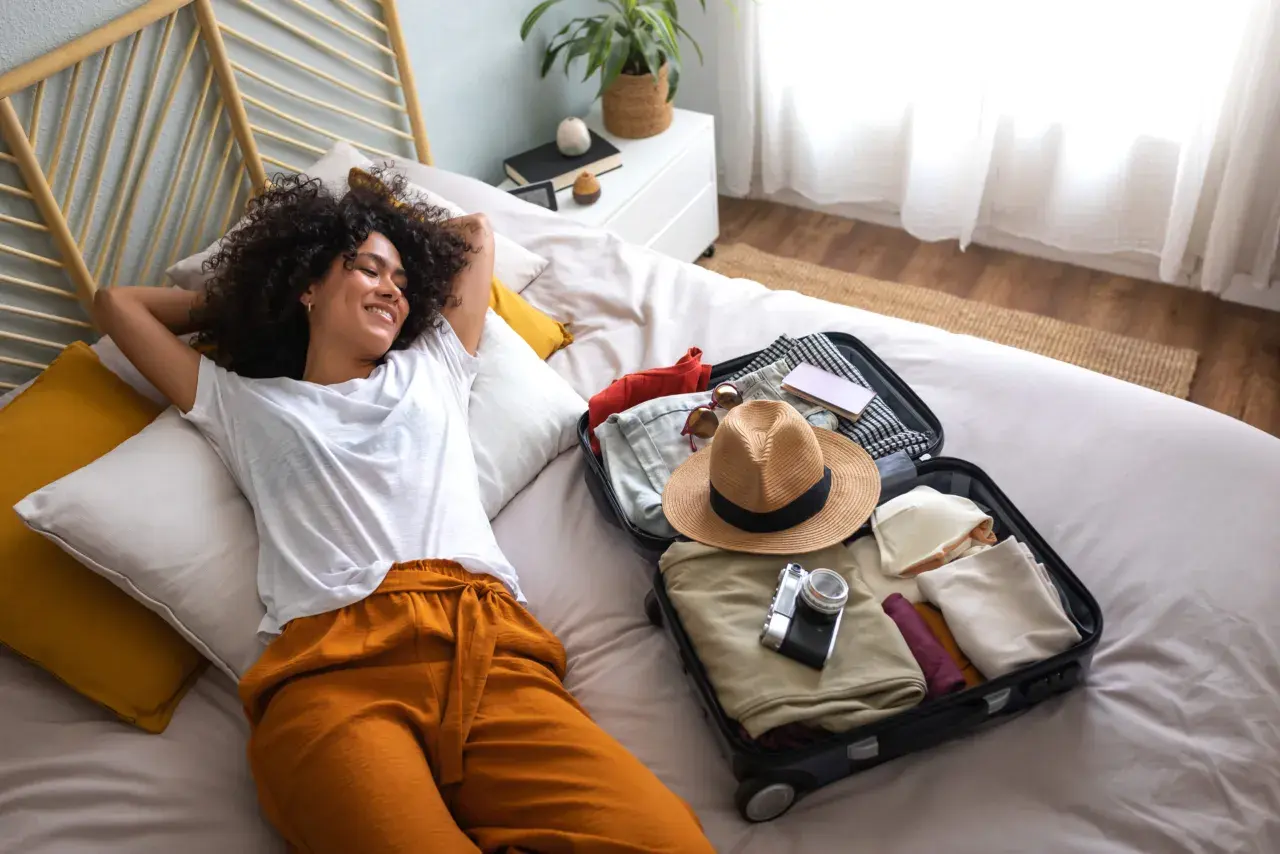 Une jeune femme se détend sur un lit, une valise ouverte à côté d'elle, prête pour son voyage. Elle est le parfait médiateur du tourisme, rêvant de nouvelles aventures.