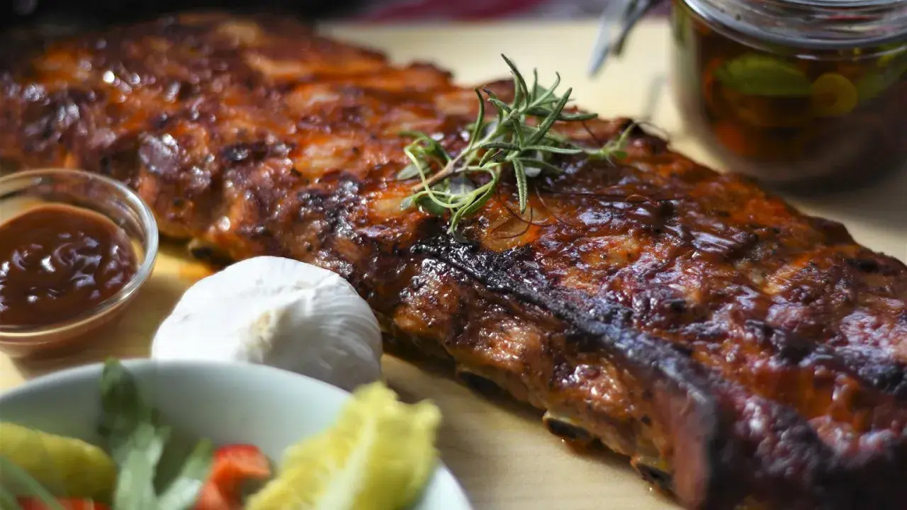 Soczyste żeberka w piekarniku, idealne do marynaty. Obok sos BBQ, czosnek i świeże zioła.