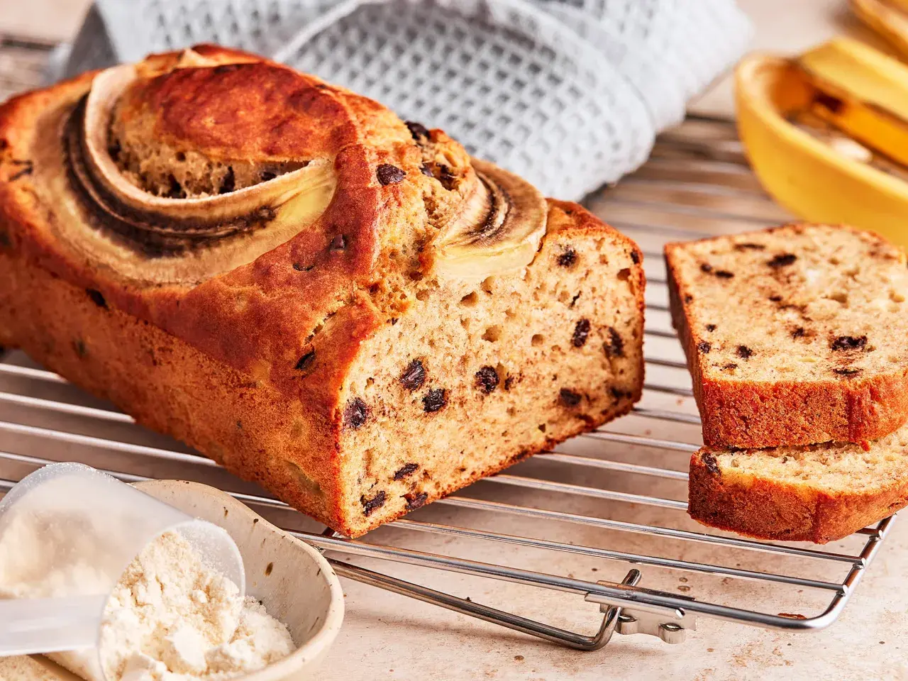 Saftiges protein bananenbrot mit Schokostückchen und Bananenscheiben, daneben eine Schüssel mit Proteinpulver.