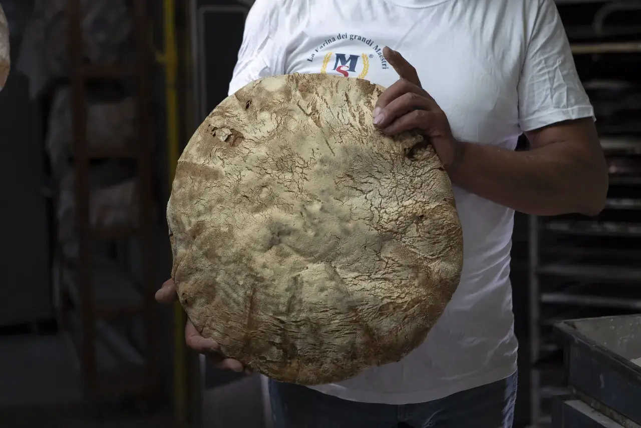Un fornaio mostra un grande pane rustico, la cui crosta ricorda la ricetta del pane di Monte Sant'Angelo.