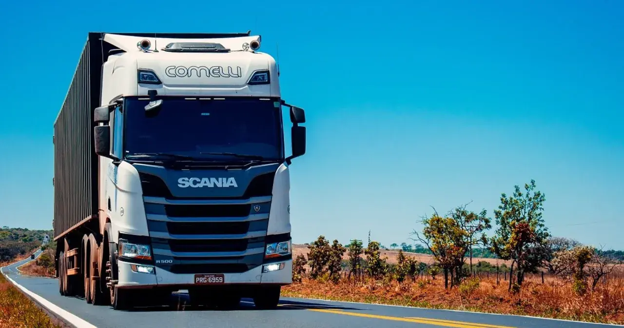 Biała ciężarówka Scania z naczepą jedzie po pustej drodze, zapowiadając zasłużoną pauzę weekendową.