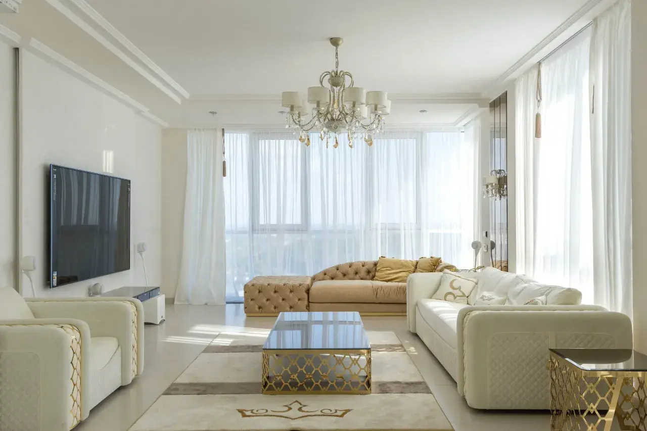 Elegancki salon w stylu nowojorskim, z jasnymi sofami, złotymi akcentami i kryształowym żyrandolem.
