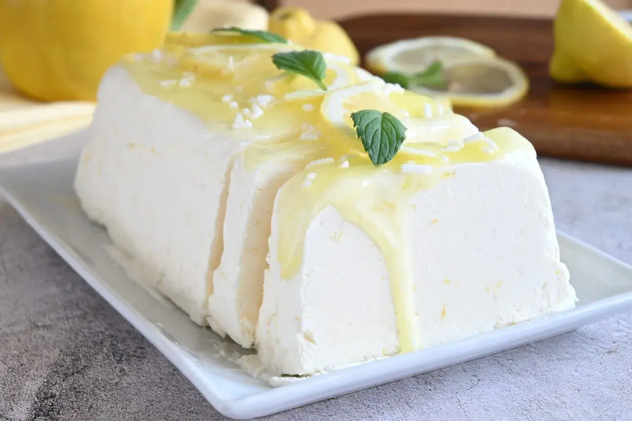 Un delizioso semifreddo al limone, guarnito con scorzette, menta e una glassa gialla, pronto per essere gustato.