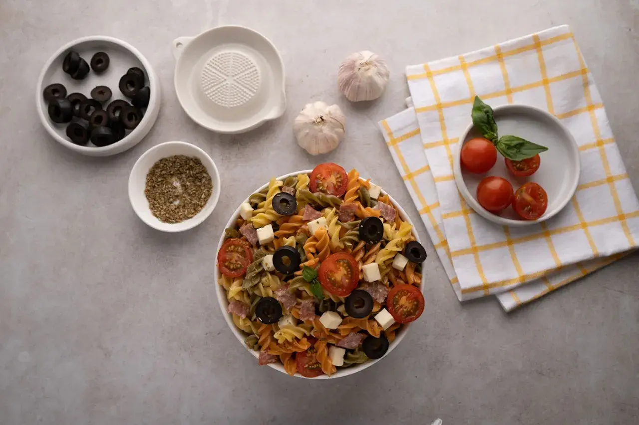 Deliciosa ensalada de pasta italiana con tomates, aceitunas, queso y salami. Ingredientes frescos listos para servir.
