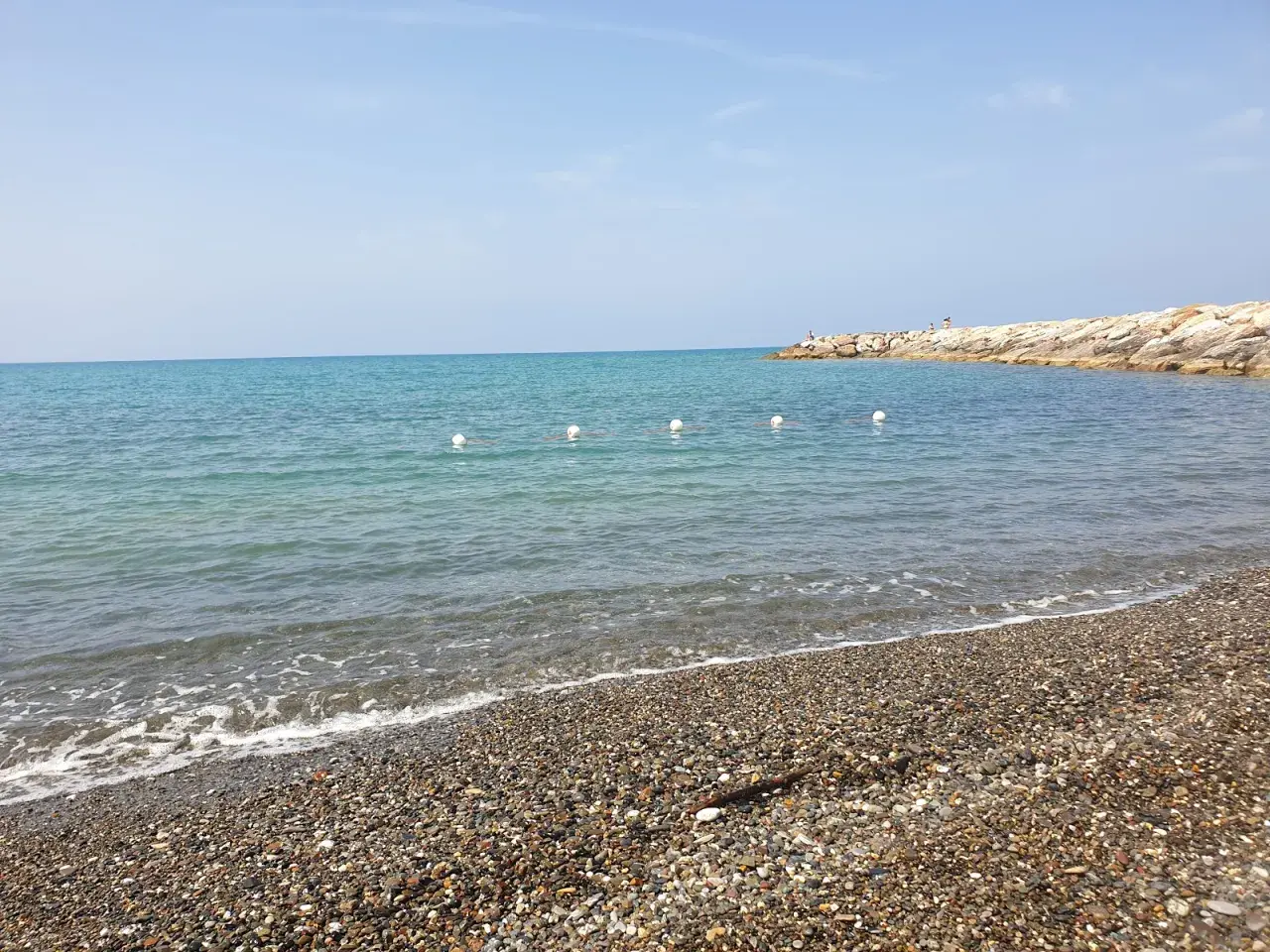 Spiagge più belle della Marina di Cecina: mare azzurro, ciottoli levigati e un molo roccioso con qualche bagnante.