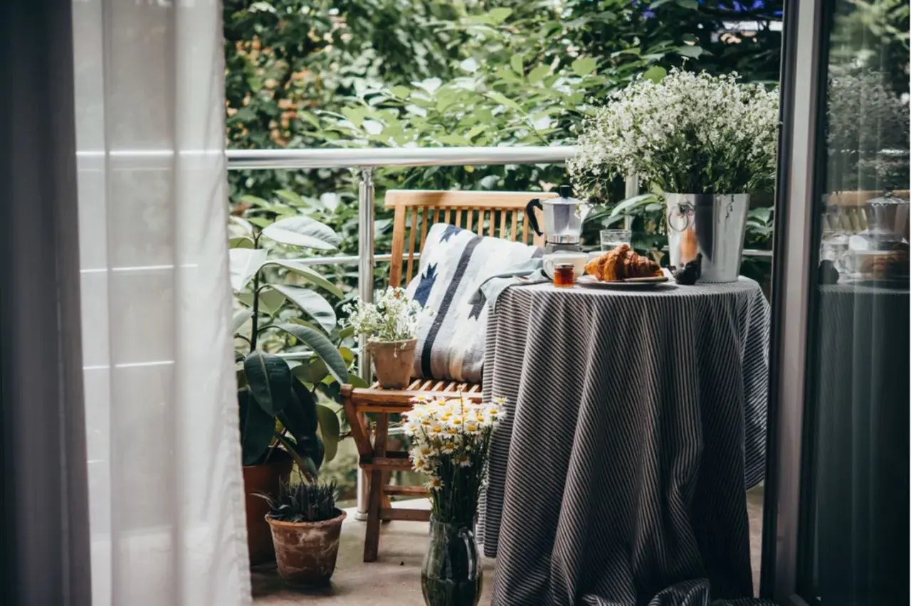 Gemütlich einen kleinen Balkon einrichten: Frühstück mit Croissant und Kaffee auf dem Tisch, umgeben von Pflanzen.