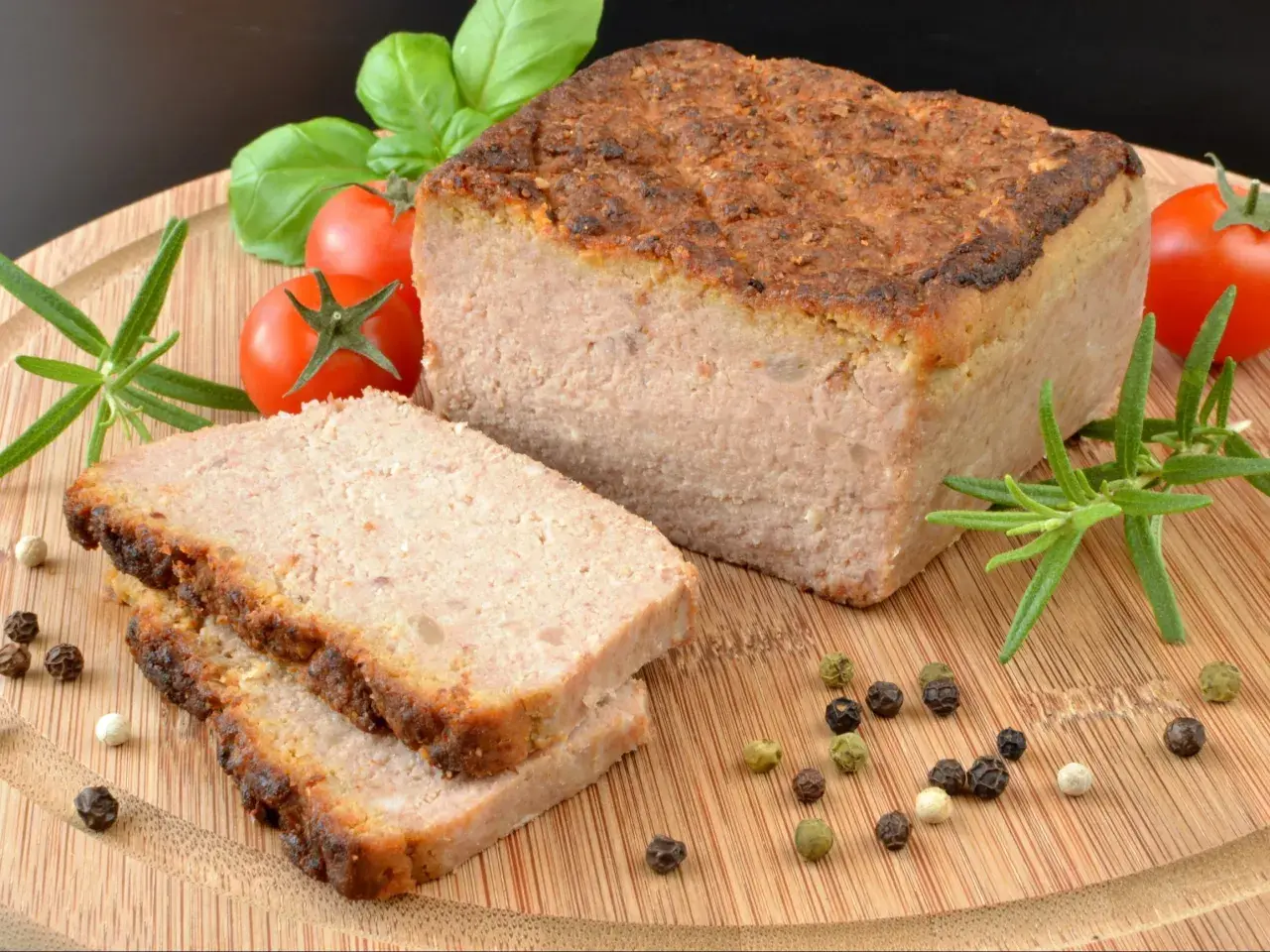 Pyszny pasztet w piekarniku, pokrojony na plastry, z pomidorkami, rozmarynem i pieprzem na desce.
