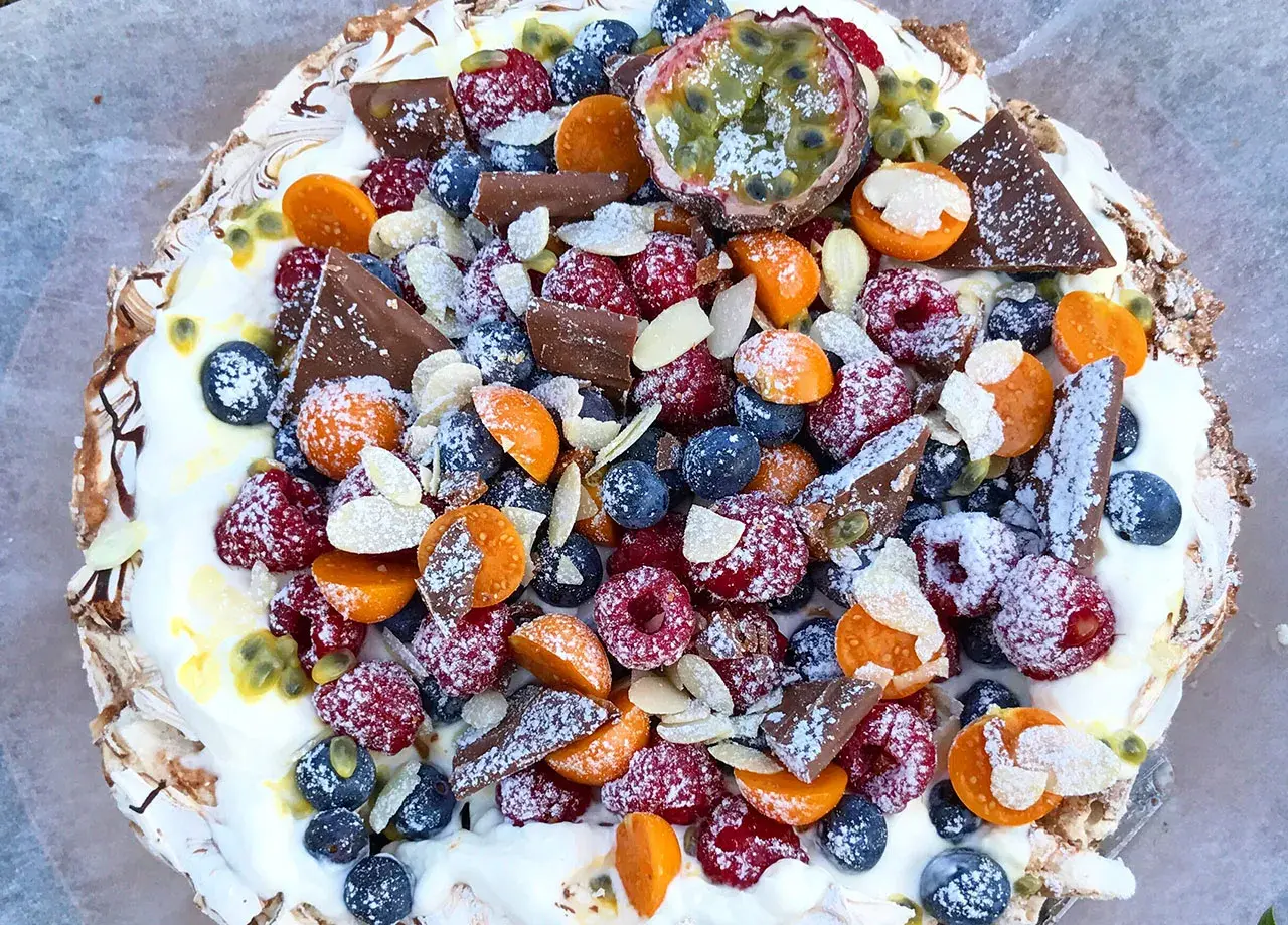 En härlig pavlova tårta fylld med färska bär, passionsfrukt, choklad och mandel.