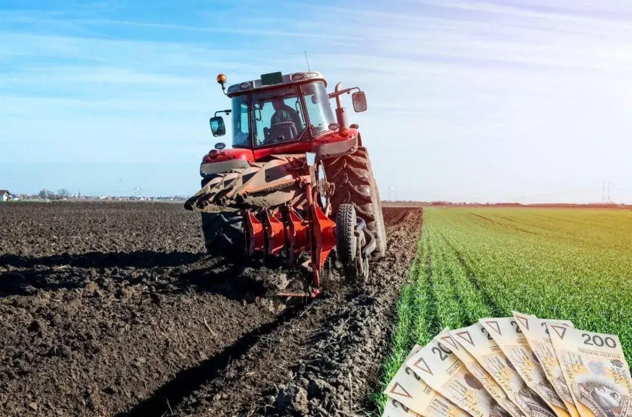 Czerwony traktor orze pole, a obok leżą polskie banknoty. Rolnicy liczą na to, że wzrosną wynagrodzenia w KRUS.