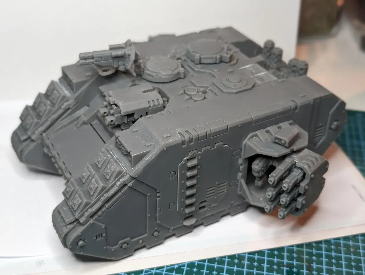 Szary model Land Raider Redeemer, gotowy do malowania, z działkiem na dachu i wyrzutniami flamerów po bokach.