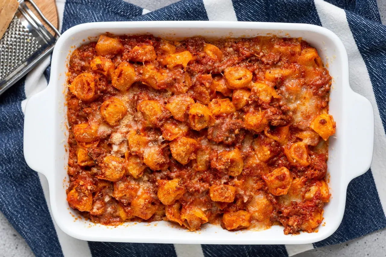 Tortelli ripieni di carne al forno, ricoperti di sugo rosso e formaggio fuso, pronti per essere gustati.