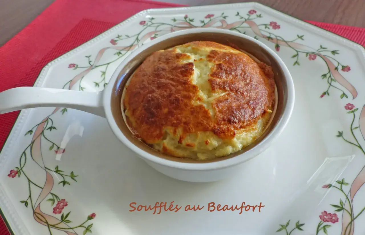 Un délicieux soufflé au beaufort, doré et gonflé, servi dans un ramequin sur une assiette décorée de rubans et de fleurs.