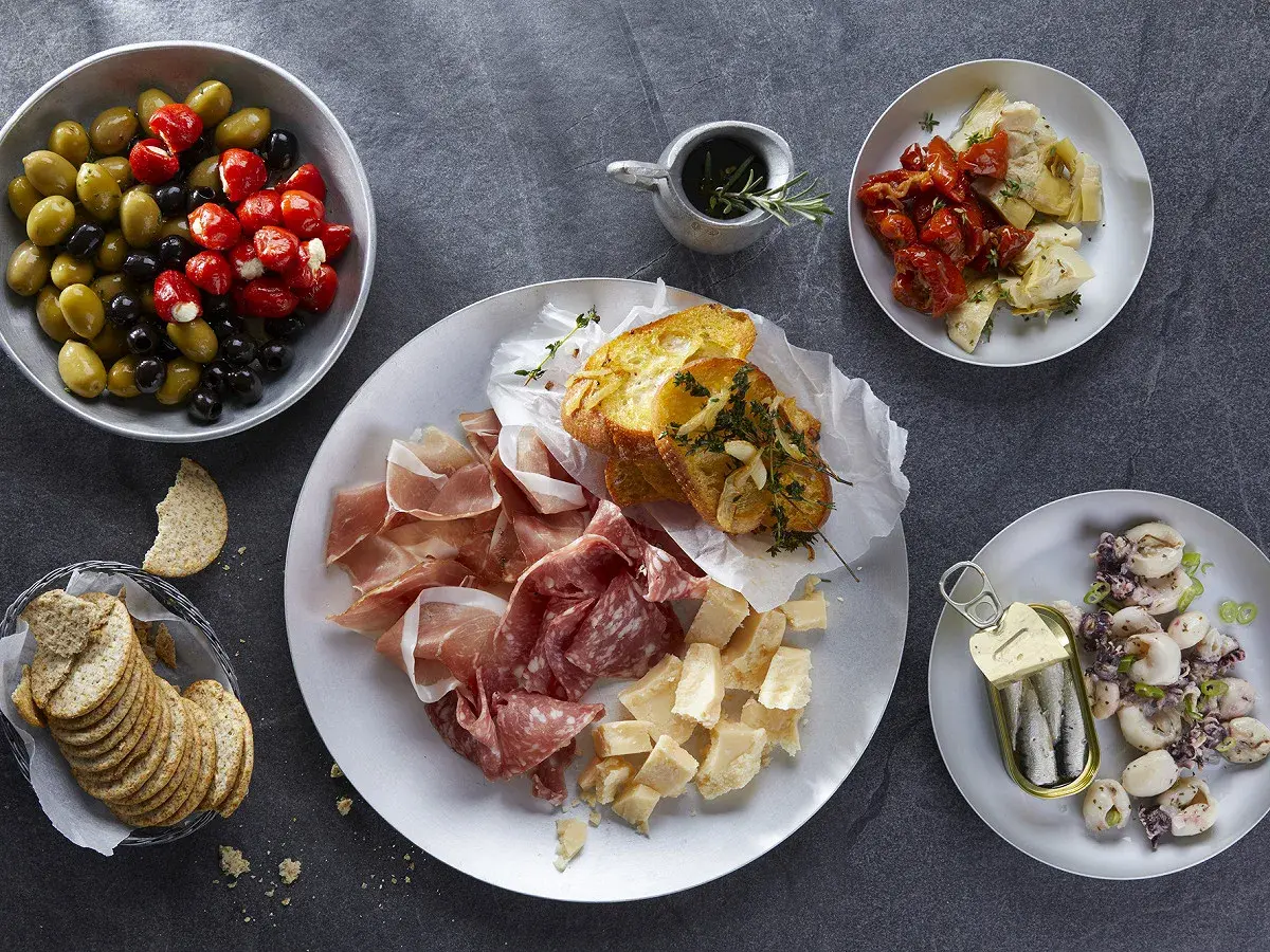 Plateau de charcuterie, fromages, olives, tomates séchées, artichauts, toasts à l'ail et sardines. Une recette antipasti italien facile pour un apéritif gourmand.