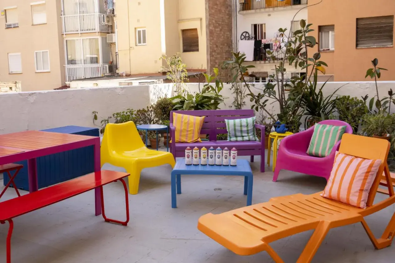 Un colorido conjunto de muebles de terraza, listo para pintar. Sillas, bancos y mesas en vibrantes tonos, con latas de spray dispuestas para dar vida a este espacio exterior.