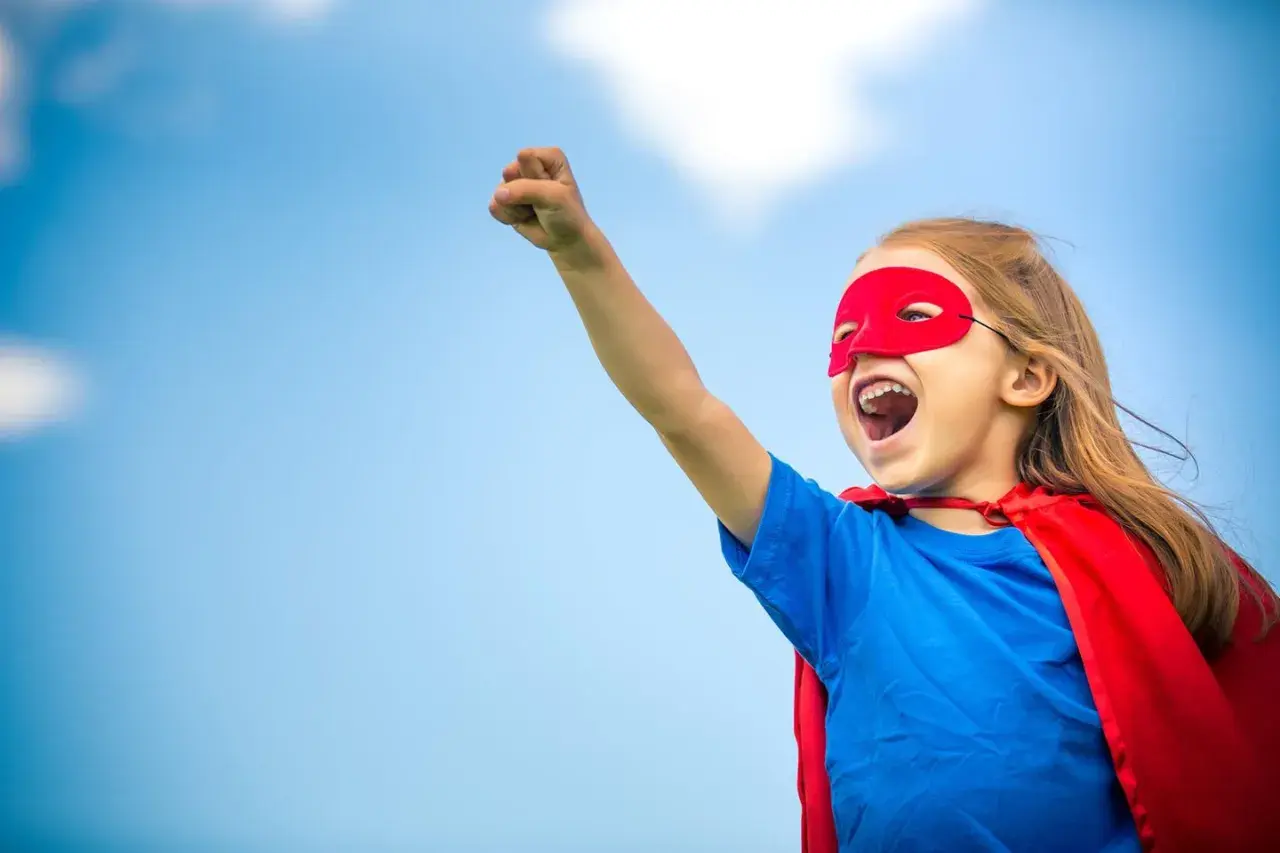 Ein Kind im Superhelden-Kostüm mit rotem Cape und Maske, bereit für den ablauf einschulung.