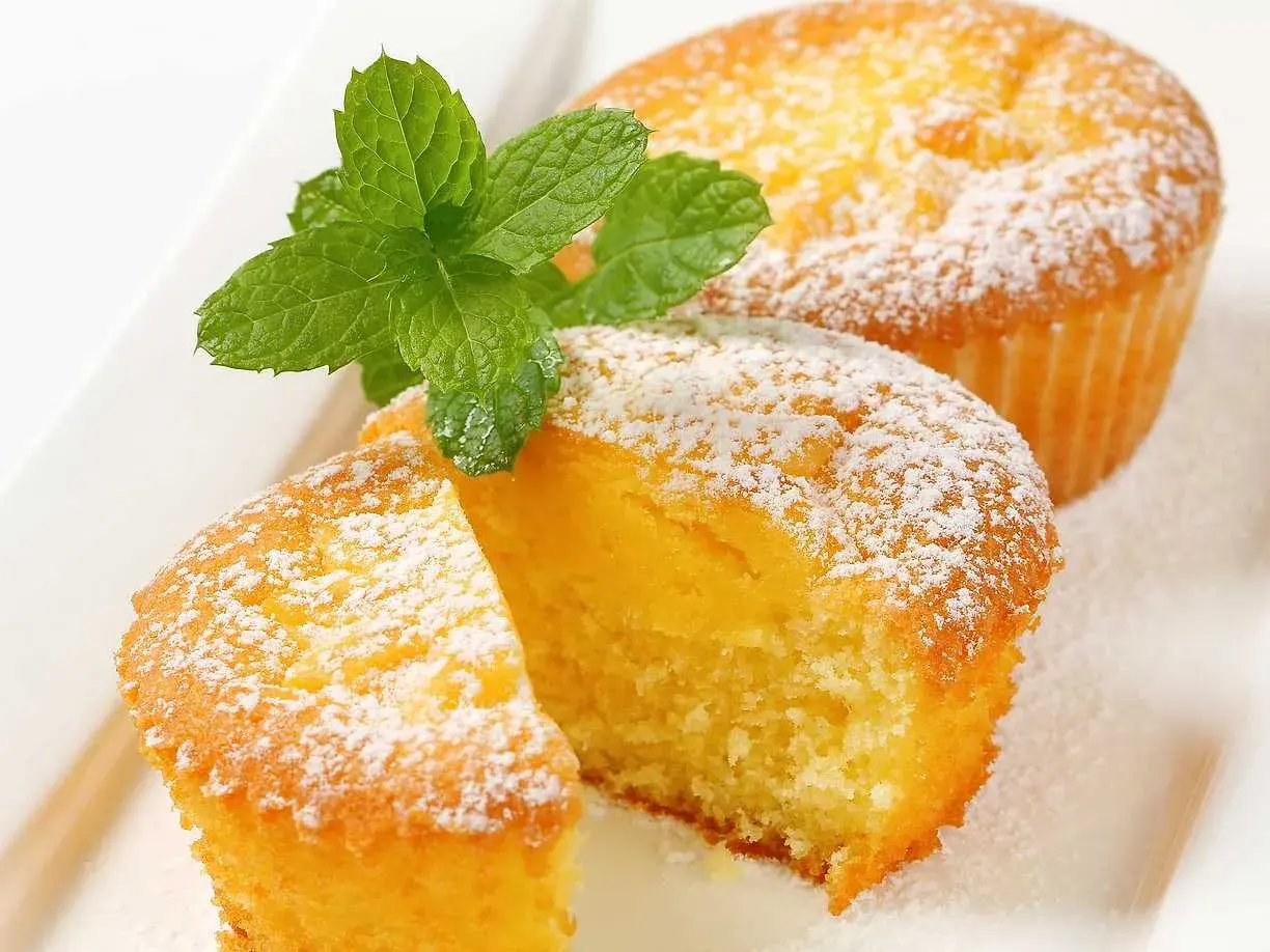 Två fluffiga citronmuffins, pudrade med florsocker och garnerade med mynta. Perfekt för ett enkelt citronmuffins recept.
