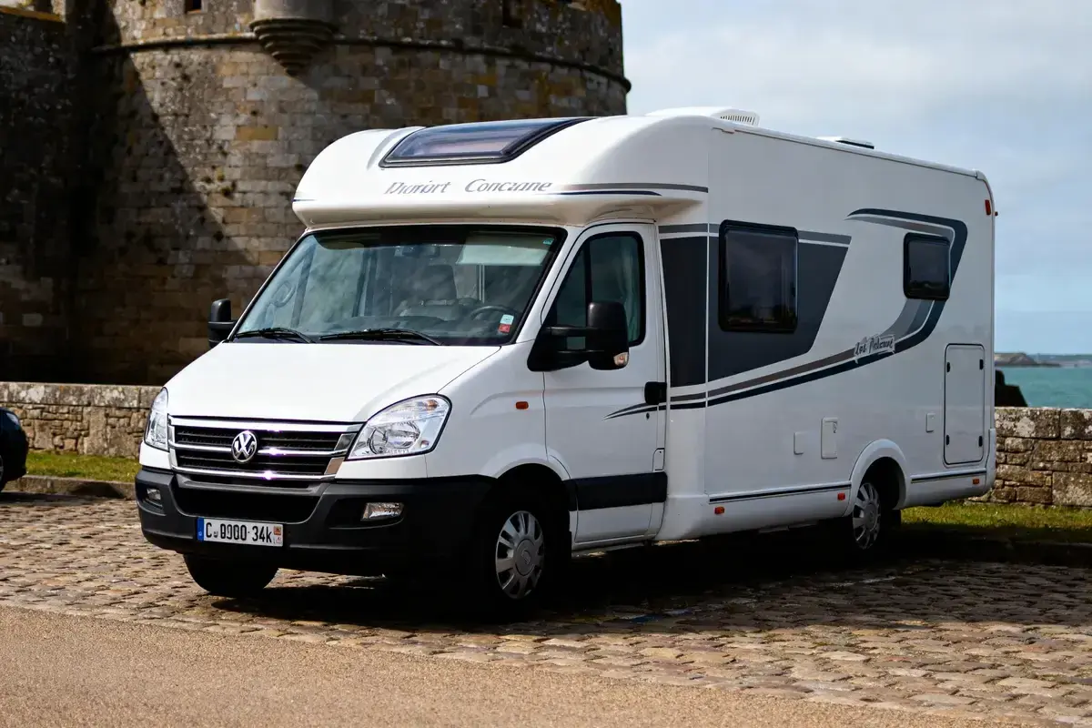 Un camping-car blanc "Dauphin Concarneau" stationné sur un sol pavé, avec un mur de pierre et la mer en arrière-plan. Un spot camping car Bretagne idéal pour explorer la côte.