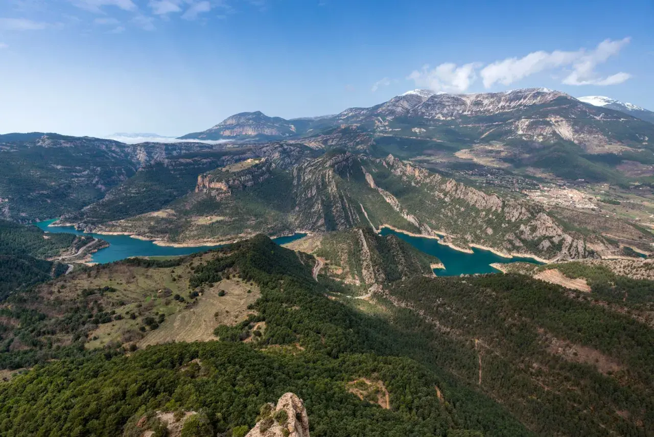 Paisaje montañoso con embalses de agua turquesa, ideal para explorar rutas Pirineos. Bosques verdes cubren las laderas y picos nevados al fondo.