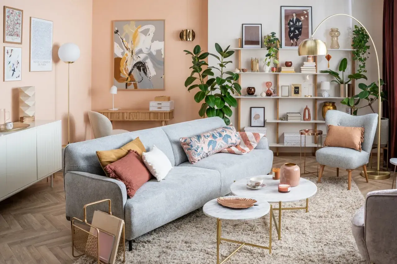 Soggiorno accogliente con divano grigio, cuscini decorativi e tavolini in marmo. Le pareti color pesca e gli arredi creano un'atmosfera rilassante, mostrando come i **colori pastello quali sono** perfetti per un ambiente sereno.